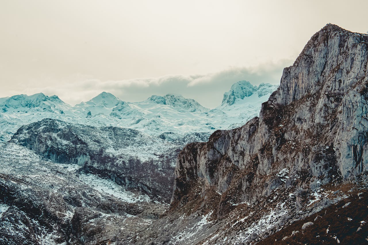 Panoramic view of snow-capped mountains under a cloudy sky, showcasing nature's grandeur.